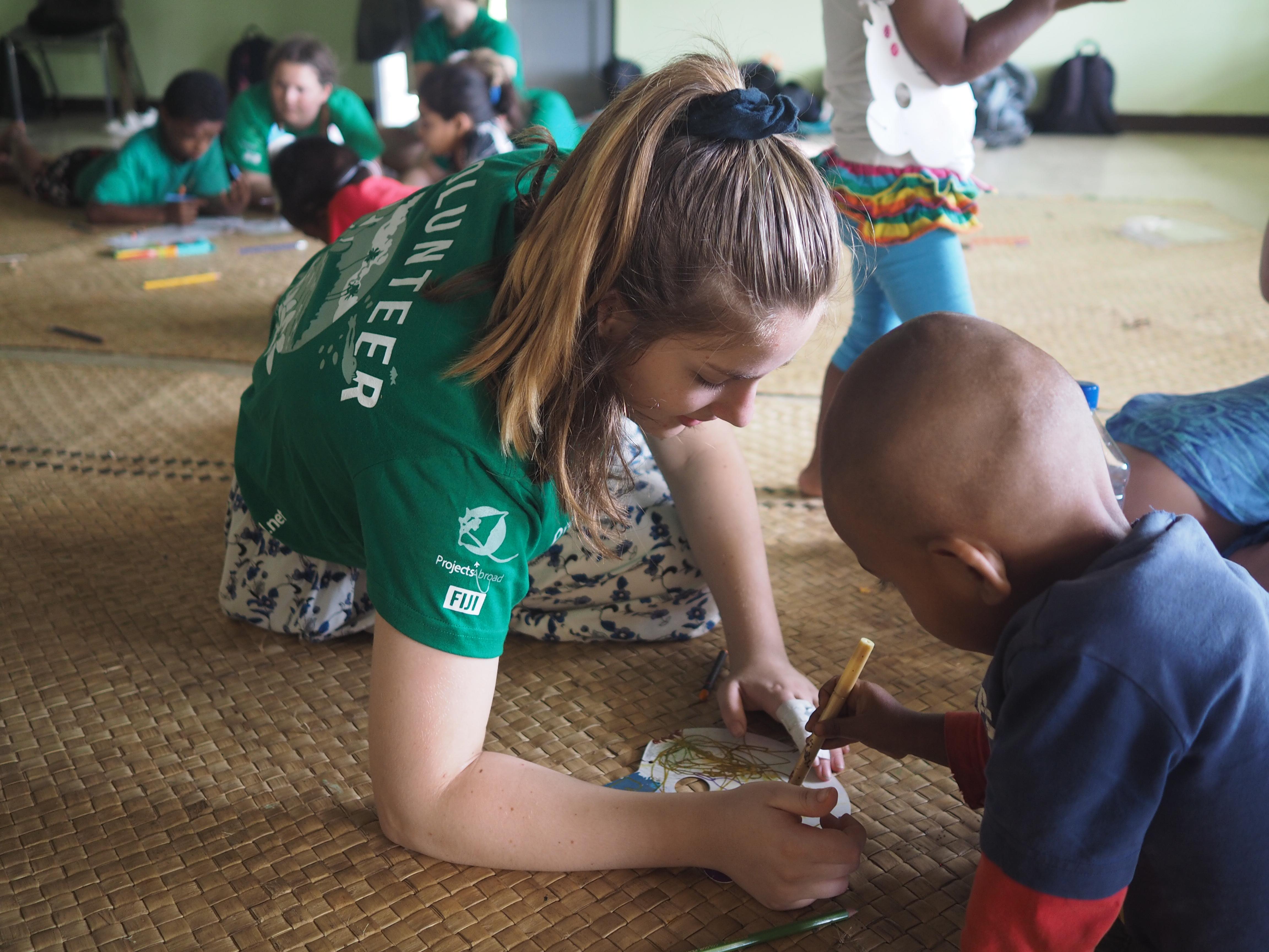A female volunteer sits in a special needs school helping a child to draw during a Childcare project in Fiji. Projects Abroad volunteer with children in Fiji sits on the floor of a special needs day school to help a child to draw during her Childcare Project.